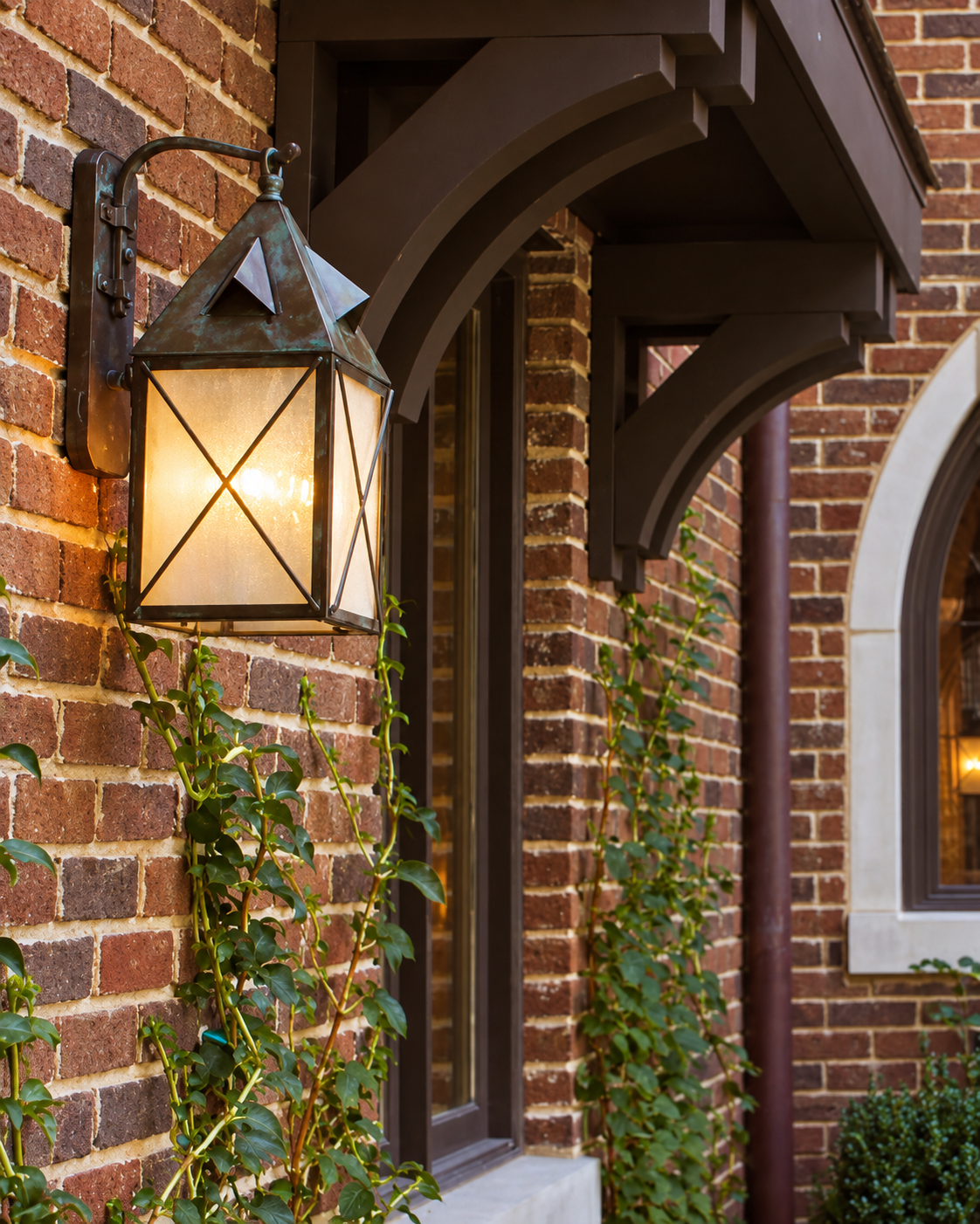Illuminated Lancaster EX-5910-A42 solid brass outdoor wall lantern with Crosscut overlay installed on a brick Tudor entry
